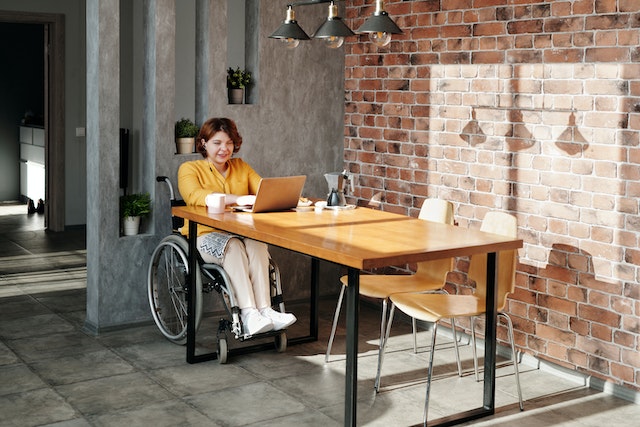 person in wheelchair typing on computer at table